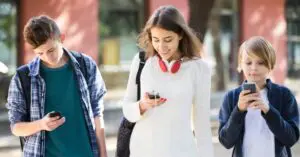 Three teens use smartphones while walking.