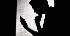 A silhouette of a teen using their smartphone.