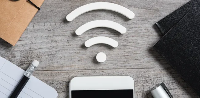 Items on a desk - notepad, diary, folders, pens and a smartphone - and the Wi-Fi connection symbol at the centre