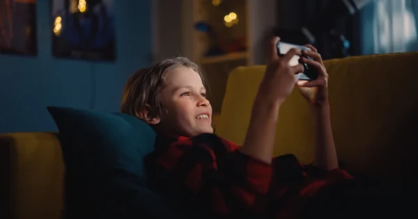 A boy laying on the sofa and watching a video on his smartphone