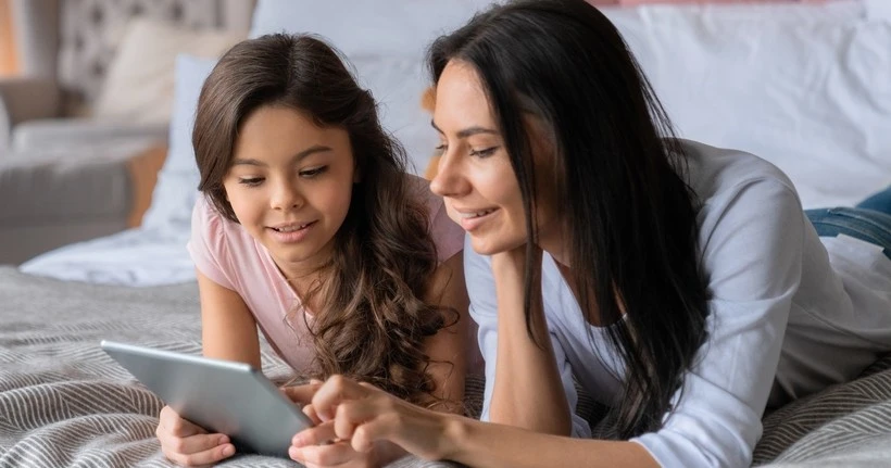 A mother and child look at a tablet while chatting.