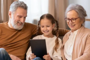 A child uses a tablet while her grandparents watch on.