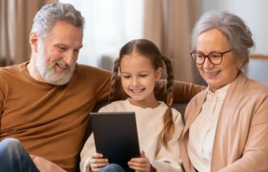 A child uses a tablet while her grandparents watch on.