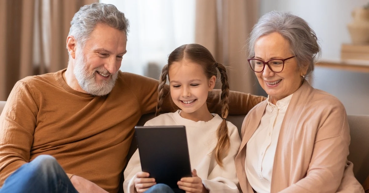 A child uses a tablet while her grandparents watch on.