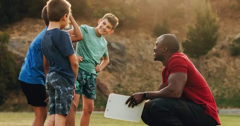 A coach crouches as he speaks with the boys he coaches.