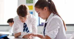 A boy and a girl in uniform, working in a classroom at school.