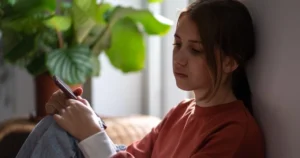 A girl sits with her phone with a sad expression.