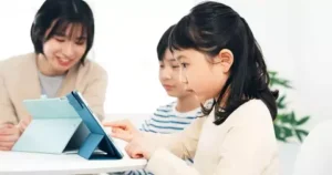 A mum sits with her two children who are watching videos on their tablets, possibly via YouTube or YouTube Kids.