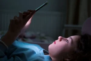 A child stares at a smartphone screen at night in their room.