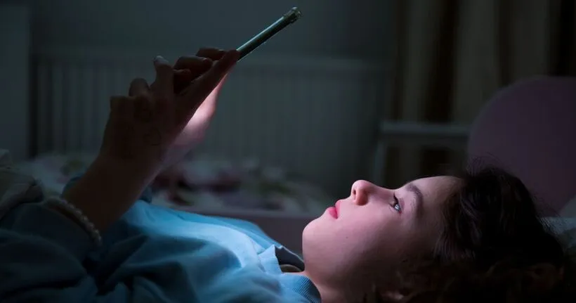 A child stares at a smartphone screen at night in their room.