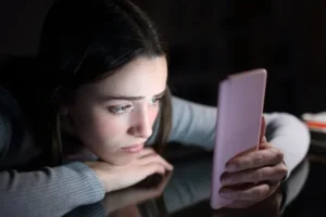 A girl in a dark room stares at her smartphone.