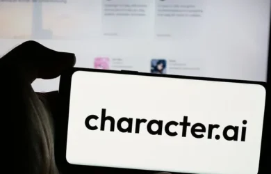 A hand holds a smartphone that reads character.ai in front of a computer screen.