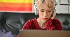 A teen wears headphones while browsing a laptop.