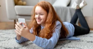 A young girl lies on her stomach browsing her smartphone.