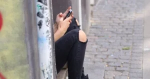 A teen sits on a step using a smartphone.