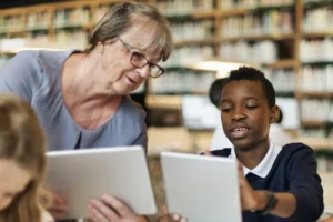 A teacher and child hold tablets while talking about what's on screen.