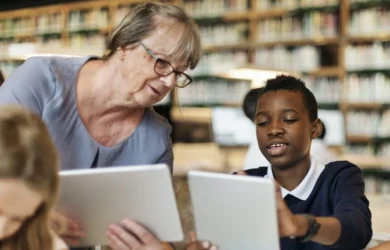 A teacher and child hold tablets while talking about what's on screen.