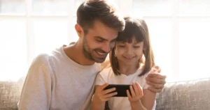 Child looking at pone with father in living room