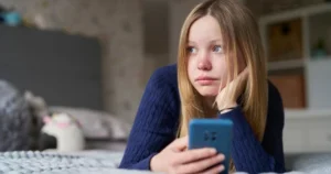 A girl looks upset and stares into the distance while holding the smartphone.