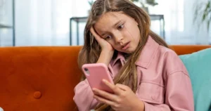 A young girl looks worried as she uses a smartphone.