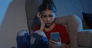 A young teen girl looks at her smartphone in the dark, worried.